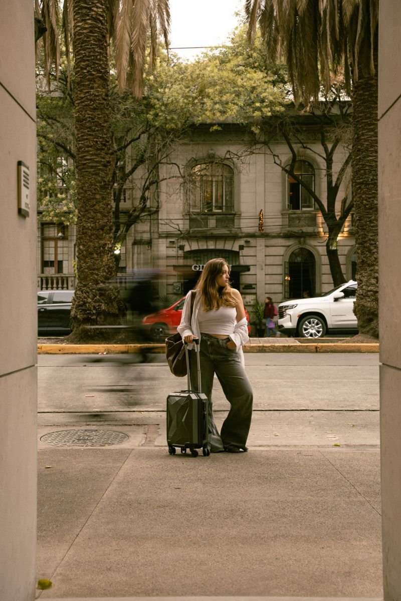 A guest arriving with her suitcase on a palm-lined street in Roma Norte